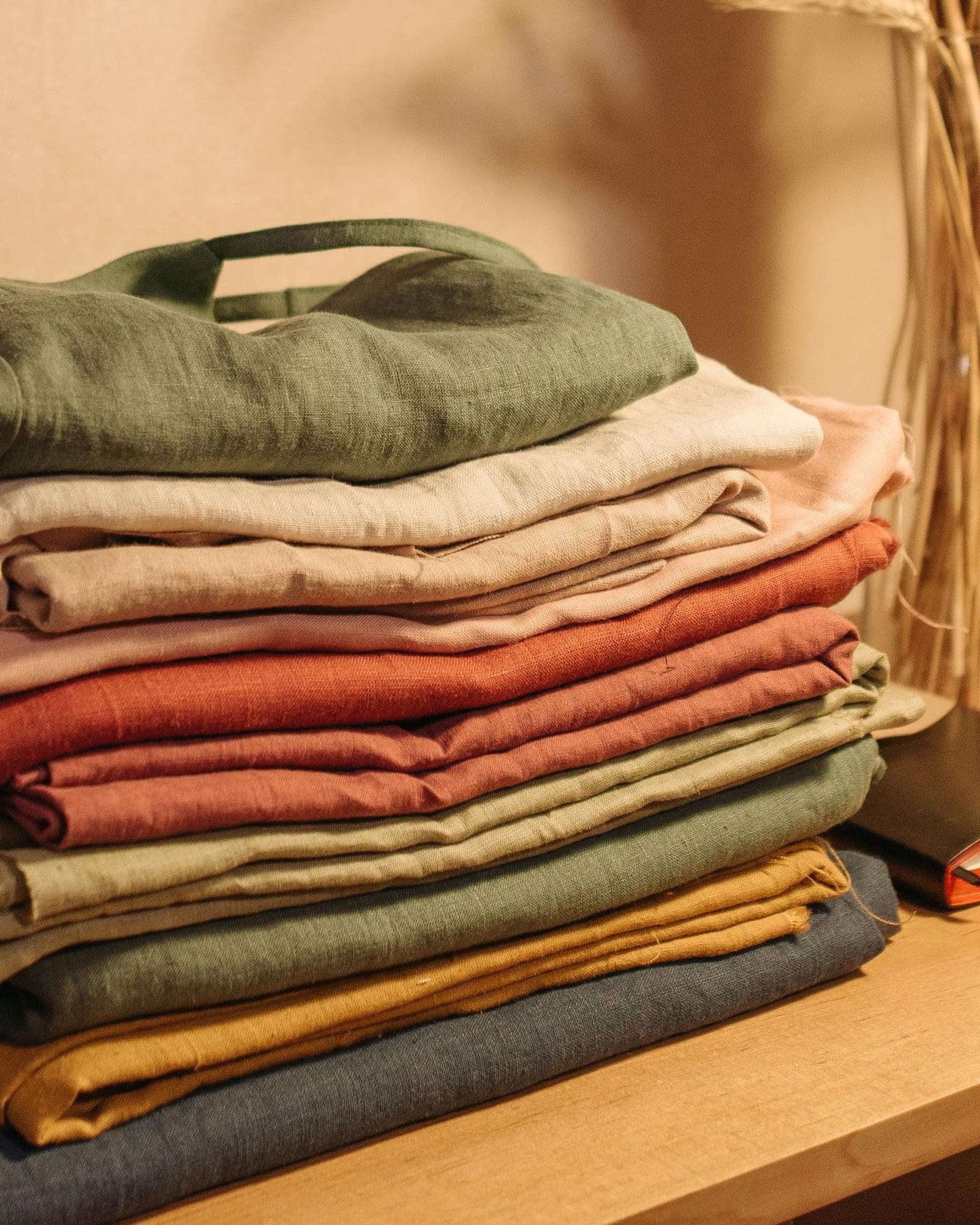 A stack of softly folded clothes in olive, terracotta and cream.
