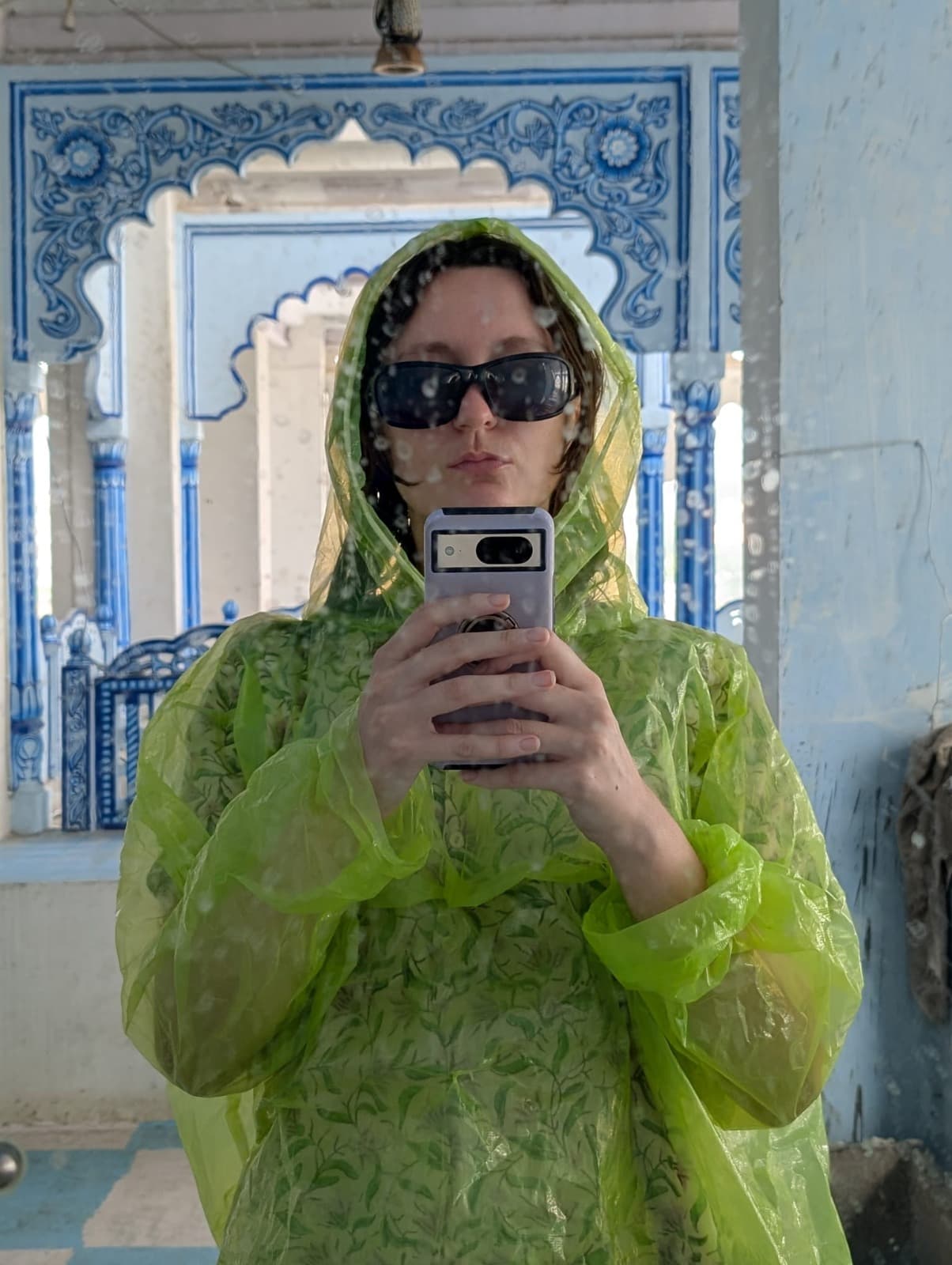 A monsoon-season selfie in a rain poncho amid blue tilework