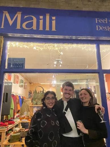 The blue Maili shopfront in Greenwich Market, lit up at night with the shop open behind